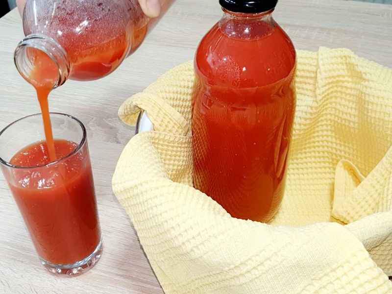 Osoba sipa sok od paradajza u čašu, pored je druga flaša soka od paradajza koja je uvijena u krpu