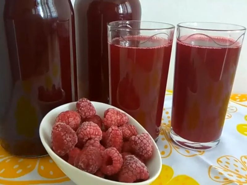 Sok od malina sipan u staklene flaše, čaša soka i činija sa malinama pored