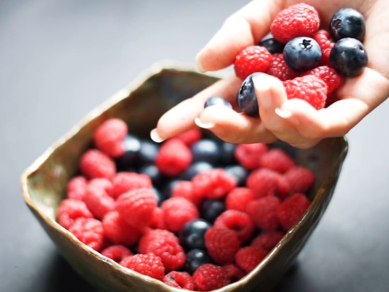 devojka drži u ruci bobičasto voće koje spušta u činiju