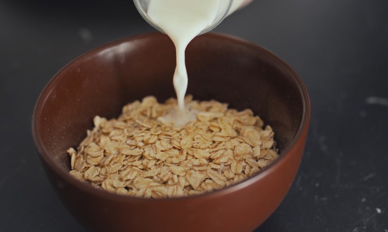 Osoba sipa mleko u činija sa ovsenim pahuljama