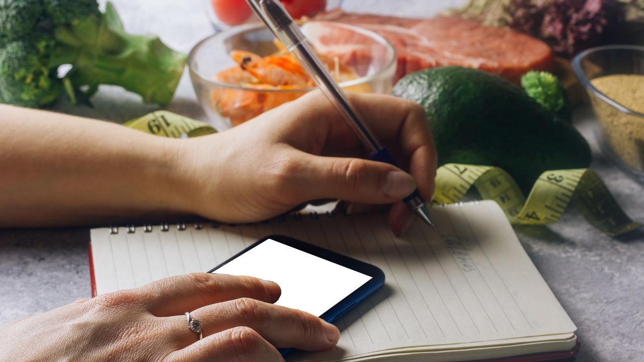 Osoba beleži unos hrane i kalorije uz telefon i namirnice kao deo plana za mršavljenje