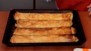 Zlatno pečeni rolati pite sa višnjama poređani u plehu nakon vađenja iz rerne