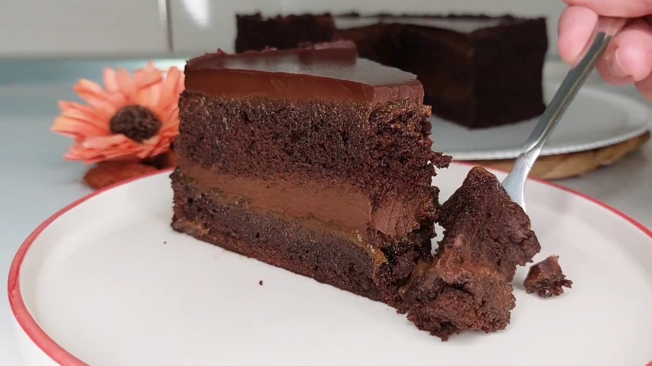 Parče bogate čokoladne torte sa kremastim filom i glatkom čokoladnom glazurom